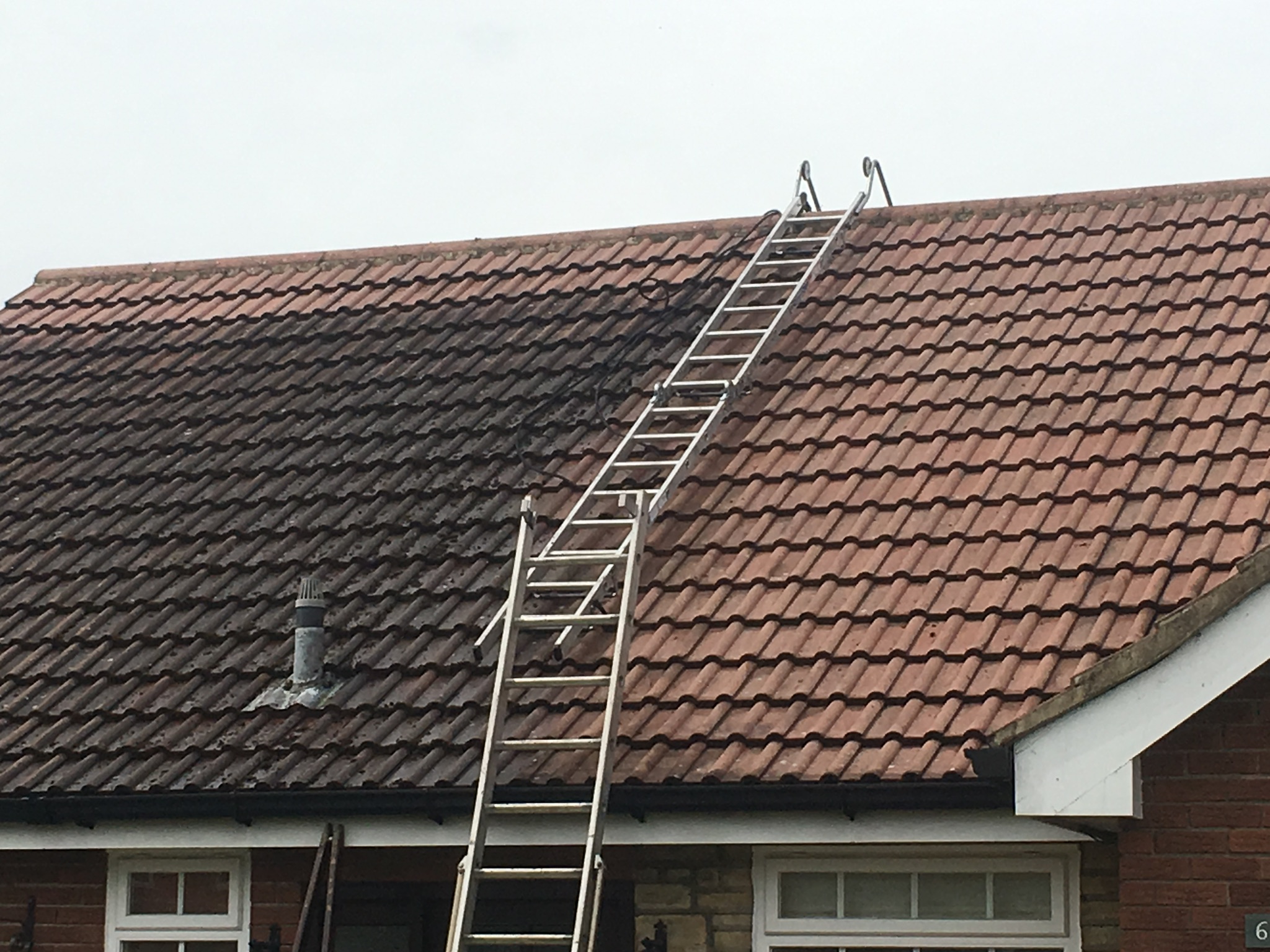 Concrete-tiled bungalow roof midway through cleaning, with dark weathered tiles beside the newly cleaned red surface