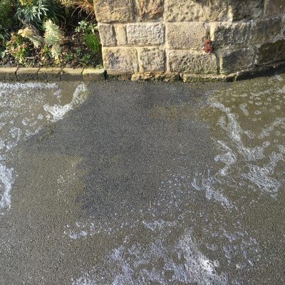 Foaming treatment working across the tarmac to lift organic staining from its textured surface.
