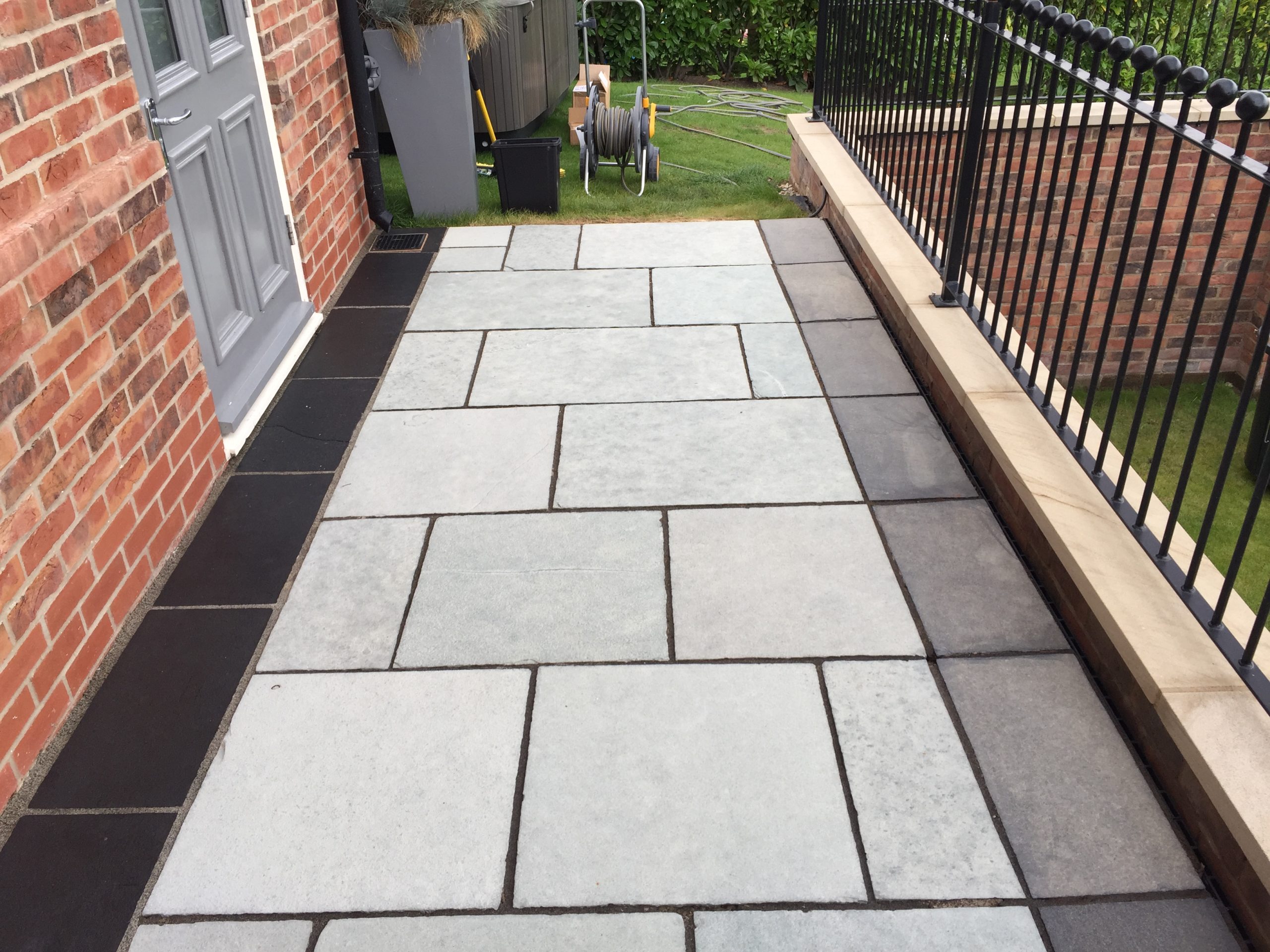 Partially cleaned black limestone border, with the dark finished section beside the house contrasting with the grey untreated slabs along the railing.