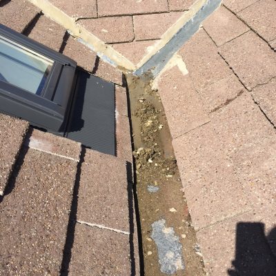 Silt, loose fragments and organic debris blocking the lead-lined roof valley beside a rooflight.