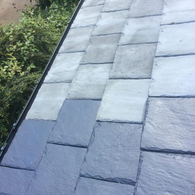 Partially cleaned natural slate roof showing its dark blue surface emerging beneath pale weathering and organic deposits.