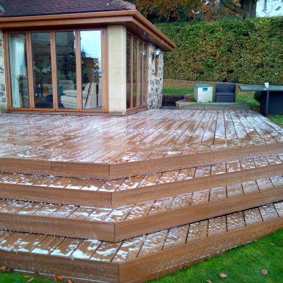 Foaming cleaning treatment spread across a multi-level composite deck and its broad steps beside a stone house.
