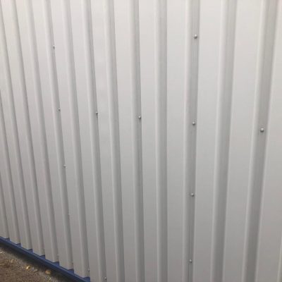 same profiled cladding after restoration, with a clean and even light-grey finish across the panels.