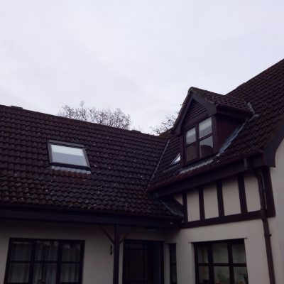 Moss and dark organic growth covering the interlocking concrete tiles of a house with dormer windows before cleaning.