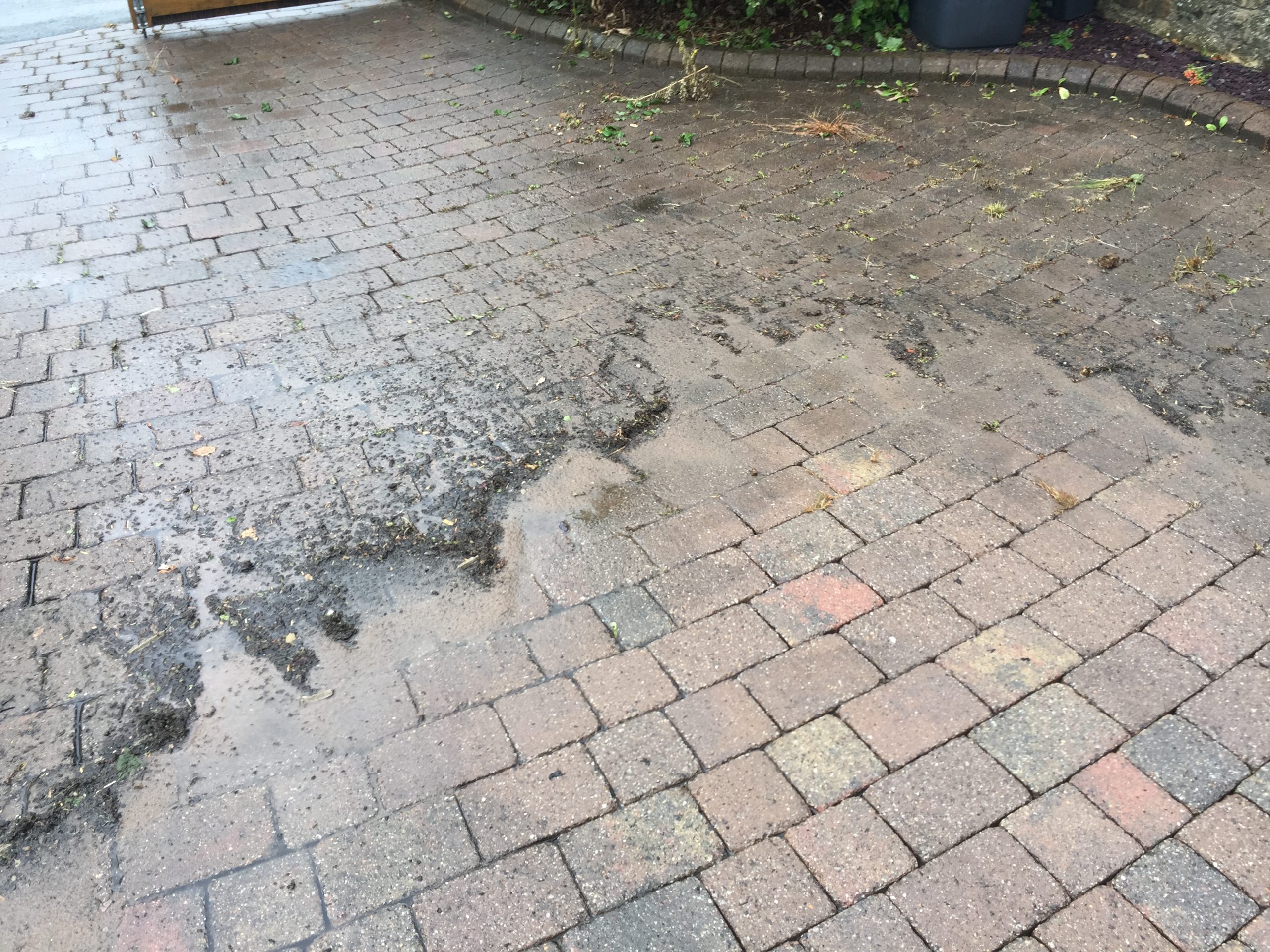 Loosened silt, weeds and organic debris being washed from a block-paved driveway during cleaning.