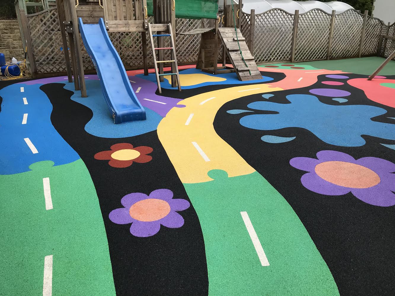 Freshly cleaned wet-pour playground surface with colourful roadways and flower designs beneath a wooden climbing frame in Leeds.