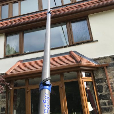 Ground-operated telescopic vacuum pole clearing third-storey gutters at a West Yorkshire home.