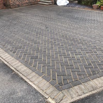 Clean charcoal herringbone block-paved driveway with freshly re-sanded joints and contrasting grey edging.