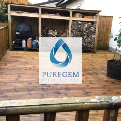 Freshly cleaned grooved timber decking in a residential garden, with organic growth and surface grime removed around the log store and planters
