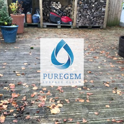 Grooved timber decking covered with green algae and fallen autumn leaves beside a garden log store before cleaning.