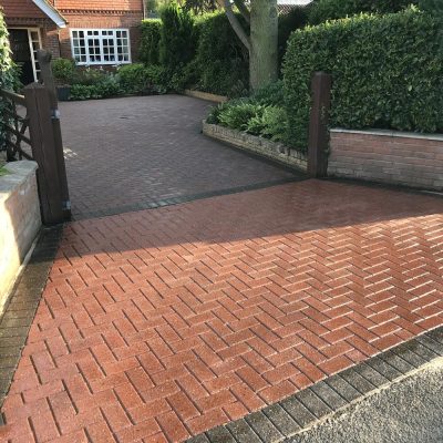 Clean red herringbone block-paved driveway with weed-free joints and contrasting charcoal edging.