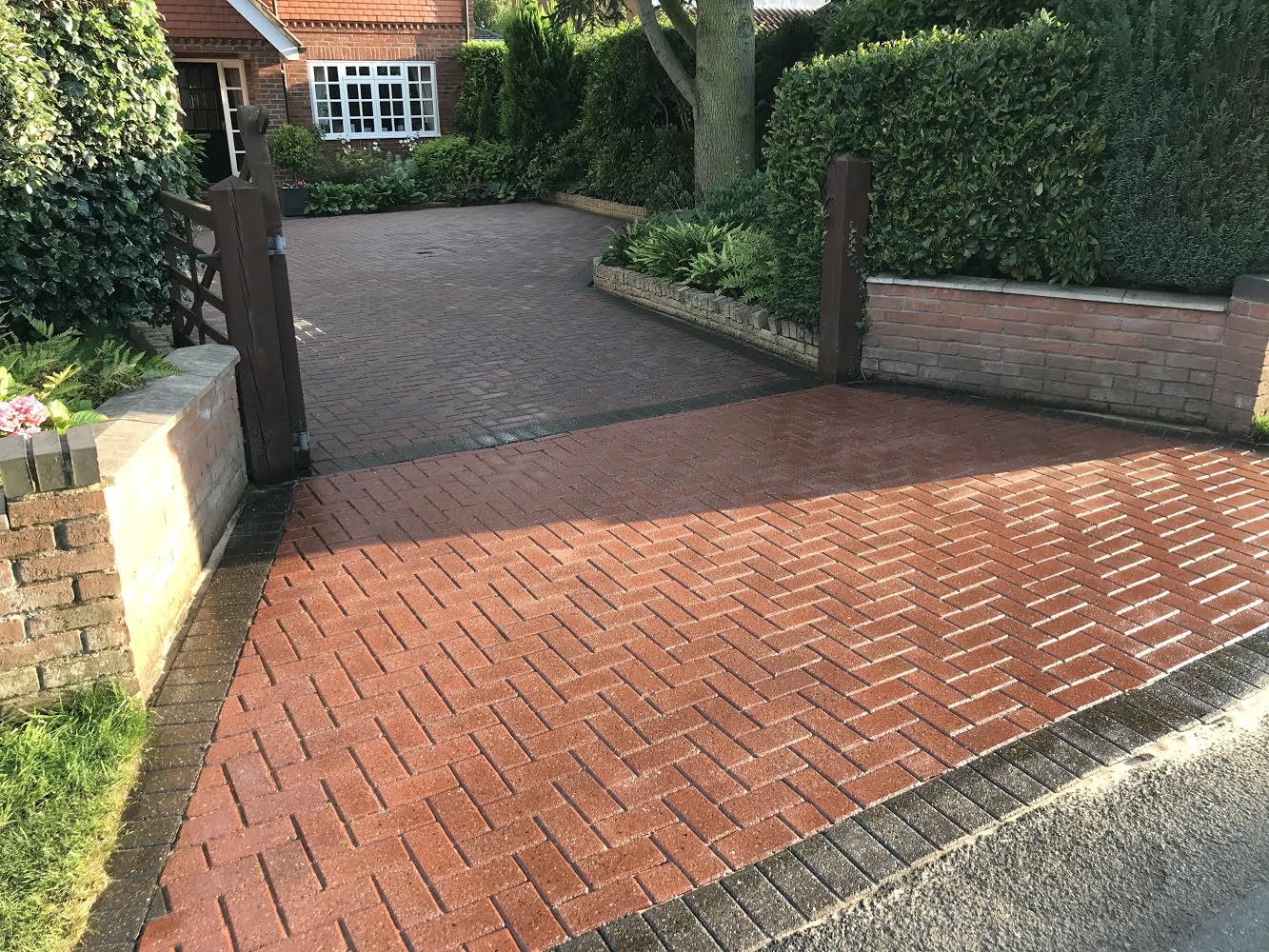 Clean red herringbone block-paved driveway with weed-free joints and contrasting charcoal edging.