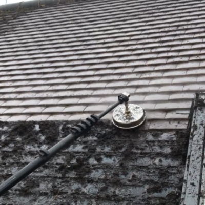 A rotary roof cleaner removing thick moss from flat concrete roof tiles beside a rooflight in West Yorkshire.
